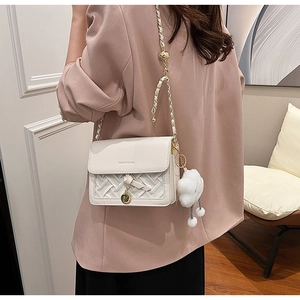 Detail of white crossbody bag with braided leather trim and a fluffy cloud pendant