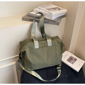 Detail view of the green nylon tote bag featuring front pocket and adjustable shoulder strap