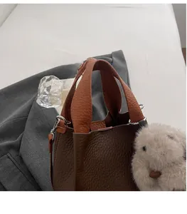 Close-up of coffee brown lychee leather bucket bag with plush rabbit charm and wide handle
