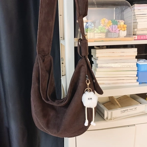 Détail du sac demi-lune en daim marron foncé avec large bandoulière et pompon en peluche