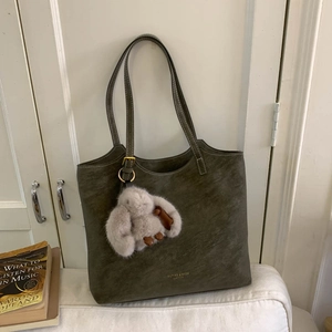 Detail of dark green matte leather tote with plush rabbit charm and white contrast stitching
