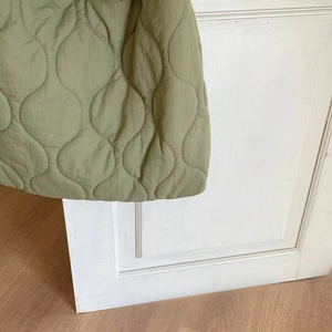 Close-up of bean green quilted nylon fabric with wavy stitching and soft texture