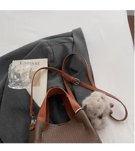 Litchi pattern bucket bag with contrast leather detail and plush charm by a gray blazer