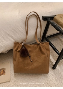 Close-up of brown leather tote bag with plush charm and logo on a vintage chair