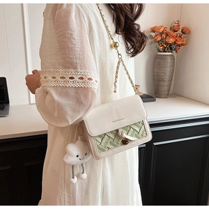 Detail of crossbody bag with green woven leather, metal lock and cloud plush charm
