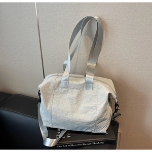 Detail of grey nylon tote bag showing wide straps and side hardware on leather sofa