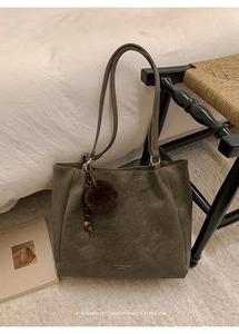 Detail of olive green leather tote bag with brown plush ball charm in a cozy indoor setting