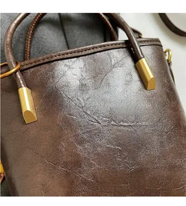Dettaglio borsa in pelle cerata marrone scuro con finiture dorate e logo inciso