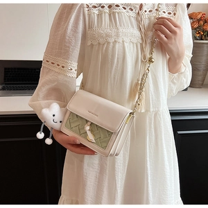 Detail of crossbody bag with beige leather, green weaving, and gold chain strap