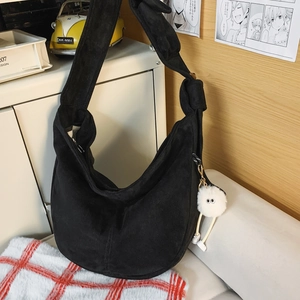 Détail d'un grand sac croissant noir en suède avec bandoulière nouée et breloque peluche