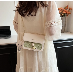 Detail of crossbody bag featuring green woven texture, gold chain and cloud charm