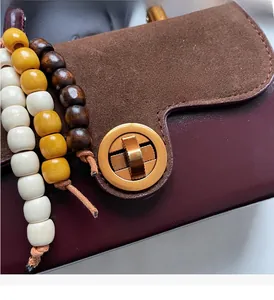 Detail of burgundy leather handbag with gold metal twist lock and colored wooden beads