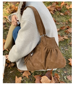 Brown suede hobo bag with silver studs and pleated texture on autumn leaf background