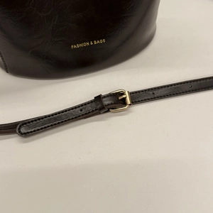 Close-up of deep brown glossy bucket bag with gold hardware and embossed lettering detail