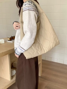 Detail view of a large beige quilted tote bag worn by a model against a minimal wall