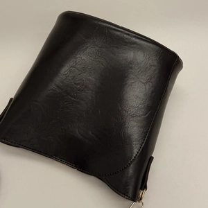 Detail of black vintage PU leather crossbody bag with glossy wrinkled texture and gold buckle