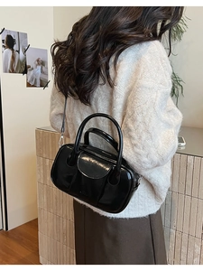 Detail of black glossy patent leather crossbody bag on a model wearing white knitwear