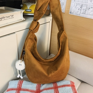 Détail d'un sac hobo en daim marron avec bandoulière nouée et pendentif pompon blanc