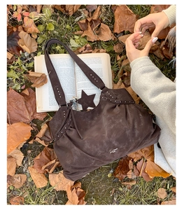 Detail of dark brown suede tote bag with silver studs and star charm on autumn leaves