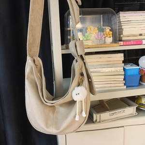 Détail d'un sac hobo mat beige avec un pendentif peluche sur une large bandoulière