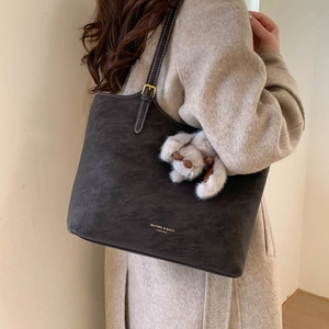 Detail of grey suede tote bag with white contrast stitching and plush puppy charm