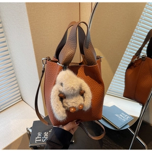 Close-up of brown litchi leather bucket bag with a plush rabbit charm on mirror