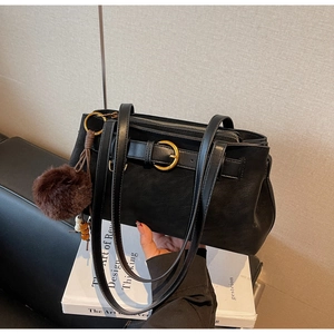 Detail of black textured leather handbag with a large gold buckle and fuzzy pom-pom charm