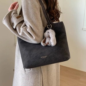 Detailed texture of charcoal grey leather tote bag with gold logo and plush bunny charm