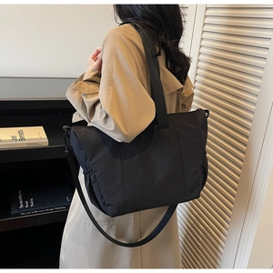 Detail of a black large capacity nylon tote bag worn over the shoulder with a trench coat