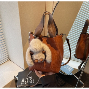 Detail of brown lychee texture bucket bag with plush rabbit charm and detachable strap