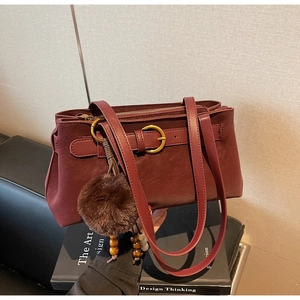 Detailed shot of burgundy leather shoulder bag with gold buckle and plush charm decoration