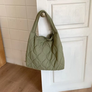 Detail of olive green quilted tote bag with wavy stitching hanging on a door handle