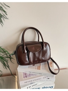 Deep brown oil wax leather bowling bag placed on magazines with pine branch decor