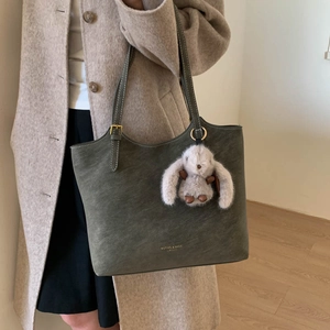 Deep grey-green matte leather tote bag detail with plush rabbit charm and brand logo