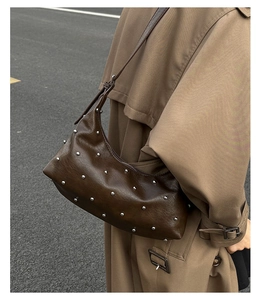Close-up of a brown leather hobo bag with silver studs on a street style model background
