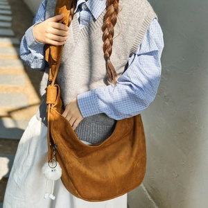 Détail du sac hobo marron en similicuir suédé avec un charmant pompon blanc sur la bandoulière