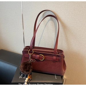 Detail of burgundy shoulder bag with decorative strap buckle and plush ball pendant charm