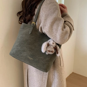Detail of grey-green tote bag with gold lettering and cute plush rabbit charm