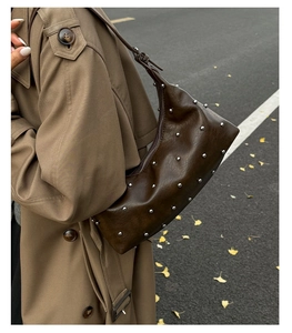 Detail of a dark brown soft leather crescent bag with silver rivet studs on shoulder
