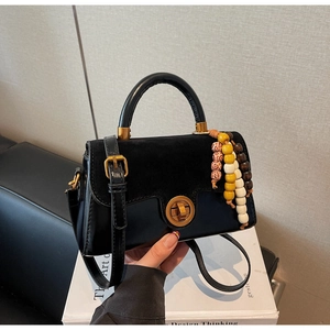 Detail of black crossbody bag with gold knob lock and colorful wooden bead ornament