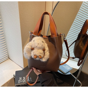 Detailed view of brown lychee leather bucket bag with orange handle and plush rabbit charm