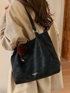 Minimalist black tote bag with plush charm and logo print shown on a model's shoulder