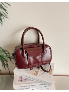 Detailed macro view of burgundy wax leather bowler bag with metallic logo and pocket