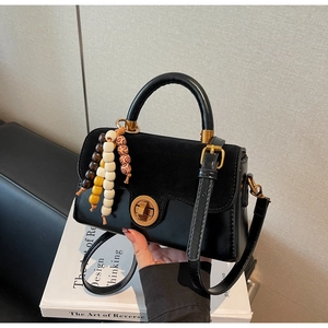 Detail of black leather handbag with suede flap, metal twist lock and wooden bead charm
