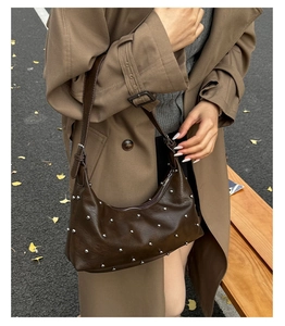 Detail of dark brown rivet dumpling bag with adjustable strap in autumn street scene