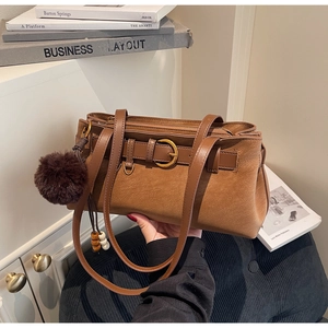Detailed view of a brown pebbled leather shoulder bag with gold buckle and pom-pom charm