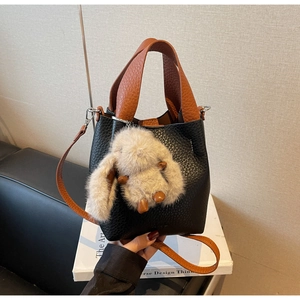 Detail of black lychee grain bucket bag with brown handles and a beige plush rabbit charm