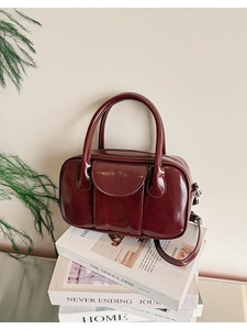 Close-up of wine red glossy bowling bag with leather handles on fashion magazines