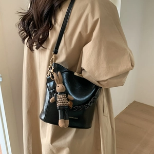 Detail of black bucket bag with gold hardware, braided chain and rabbit charm on model