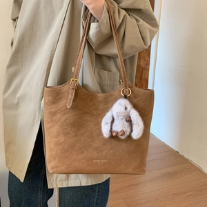 Detail of brown suede tote bag with adjustable strap and plush rabbit charm accessory